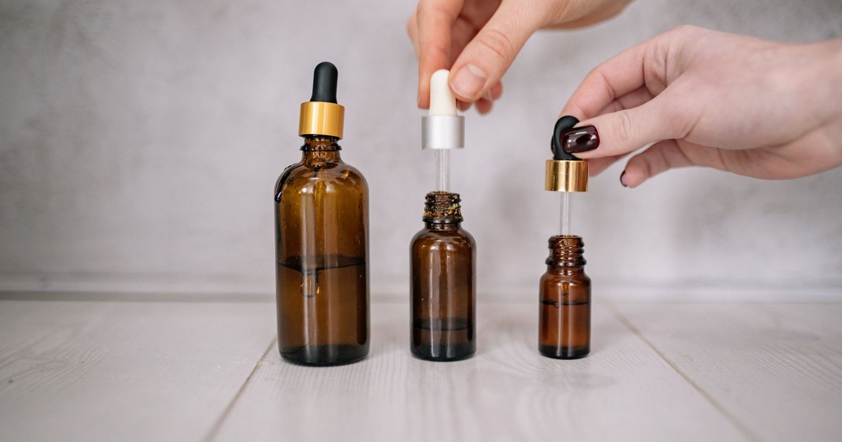 Trois flacons de sérum en verre ambré à pipette, saisis par des mains aux ongles vernis sur une table blanche