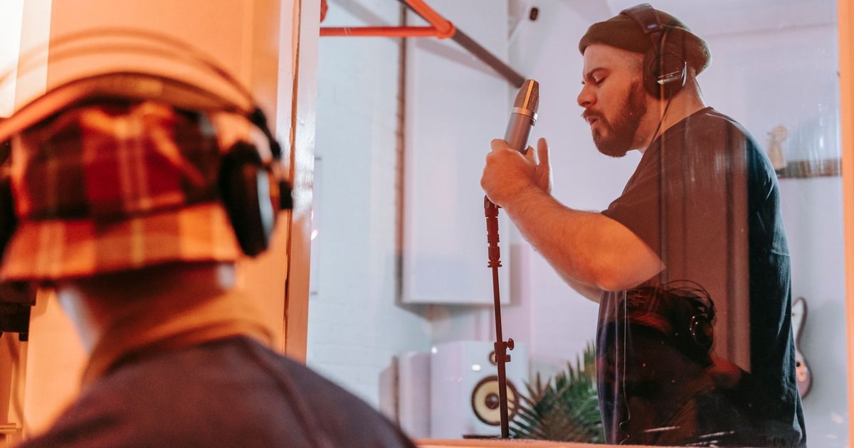 Chanteur enregistrant une voix au micro dans une cabine de studio, vu depuis la régie