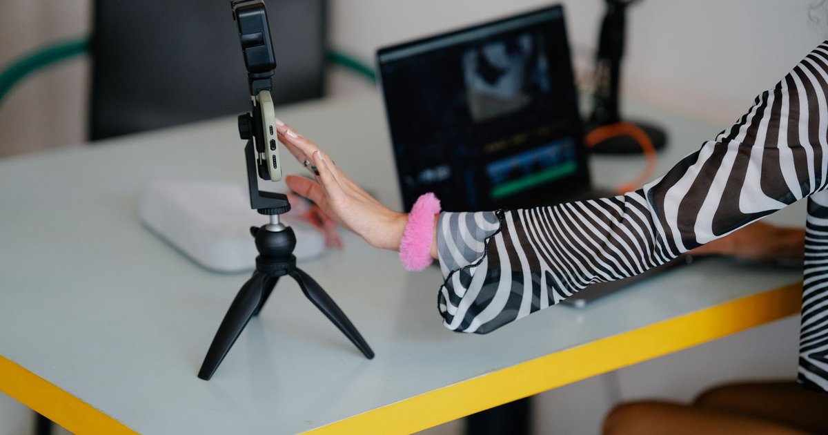 Personne assise à un bureau qui monte une vidéo verticale sur un smartphone posé devant un ordinateur portable