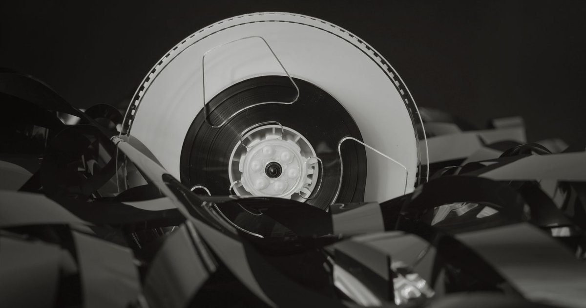 Bobine de bande magnétique déroulée sur fond noir, évoquant un catalogue d'archives audiovisuelles