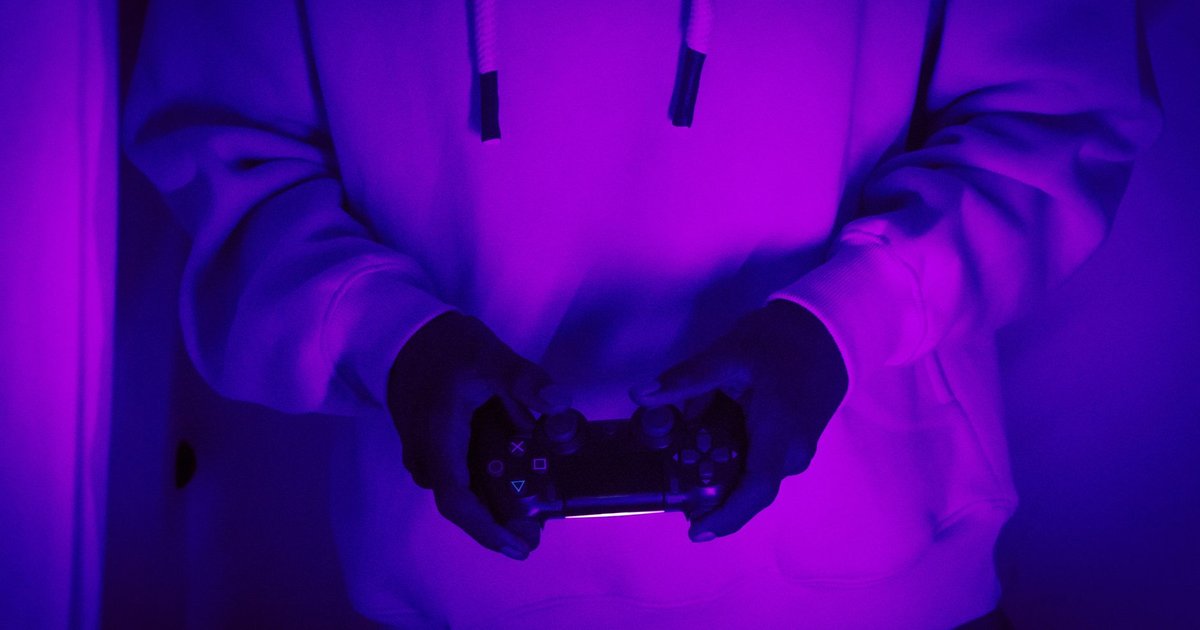 Joueur en sweat à capuche, manette de console en main, éclairé par une lumière violette néon