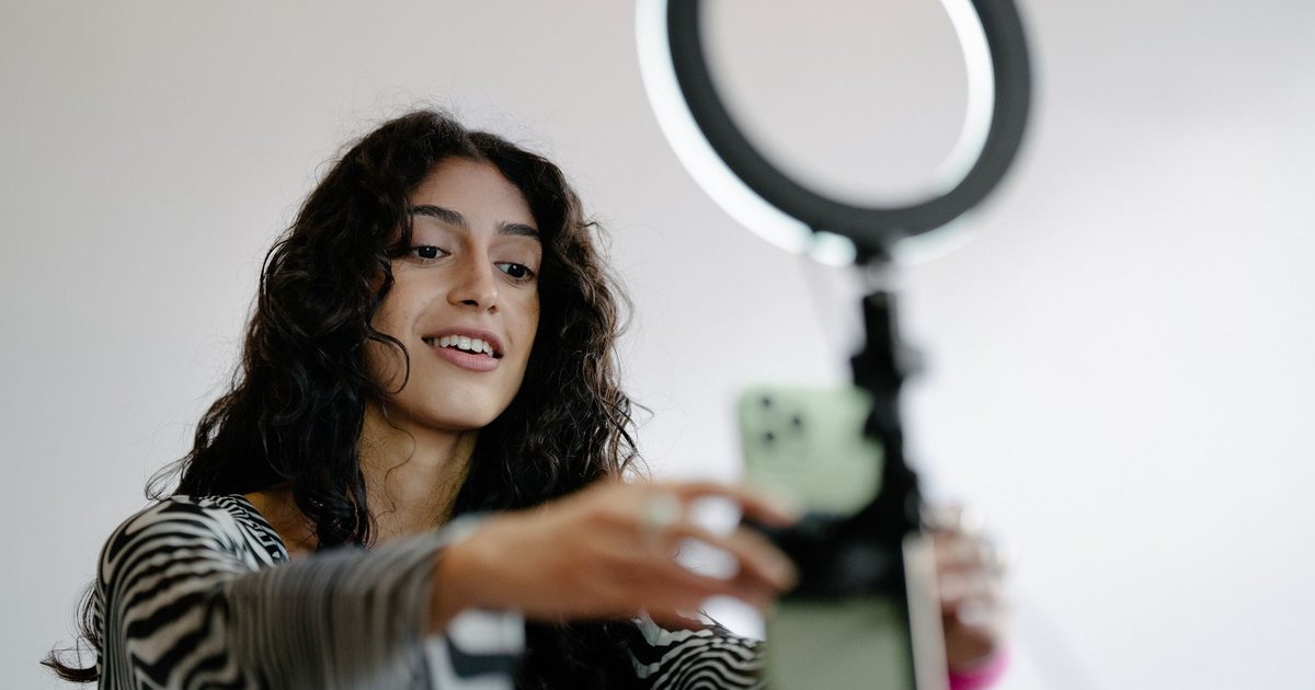 Créatrice souriante qui règle son smartphone fixé sous un anneau lumineux avant un tournage