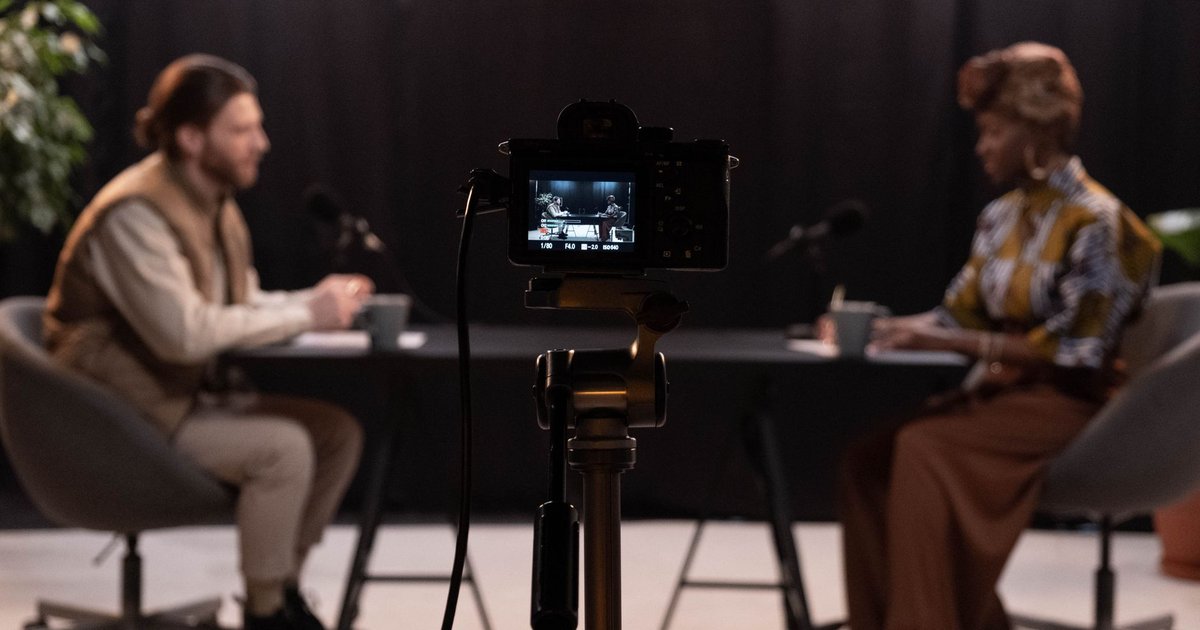 Deux animateurs assis face à face dans un studio de podcast, filmés par une caméra posée sur un trépied au premier plan