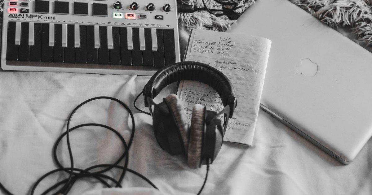Clavier MIDI, casque audio et ordinateur portable posés sur une couverture blanche pour une séance de création musicale