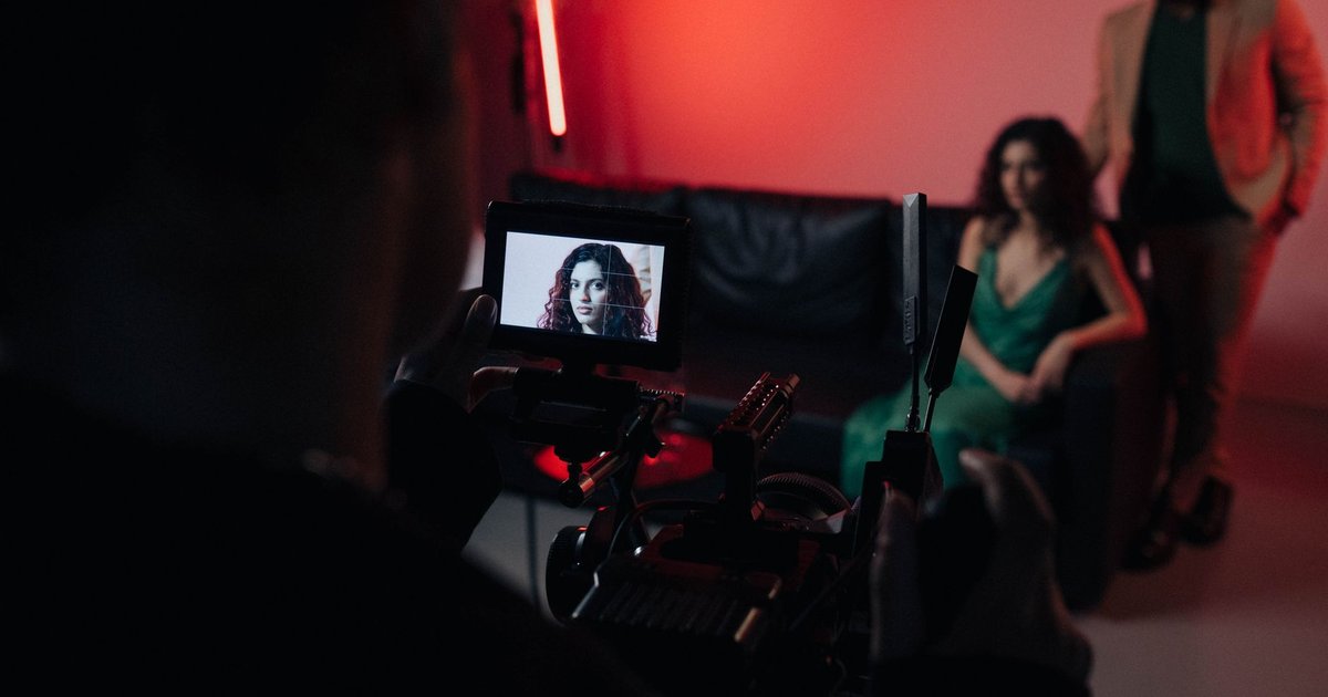 Tournage d'une scène éclairée en rouge : l'écran de la caméra cadre une actrice assise sur un canapé