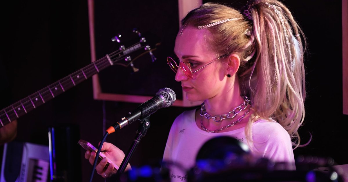 Chanteuse sur scène devant un micro, smartphone à la main, sous une lumière violette