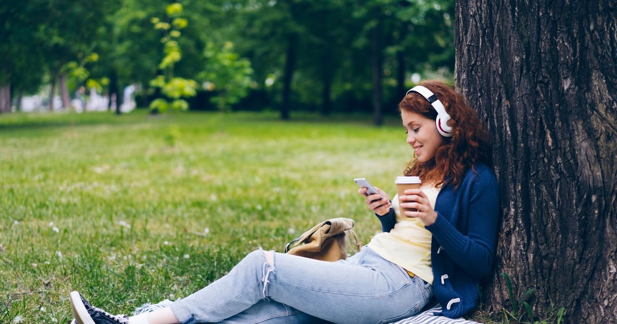 Jeune femme au casque audio écoutant de la musique sur son smartphone dans un parc ensoleillé
