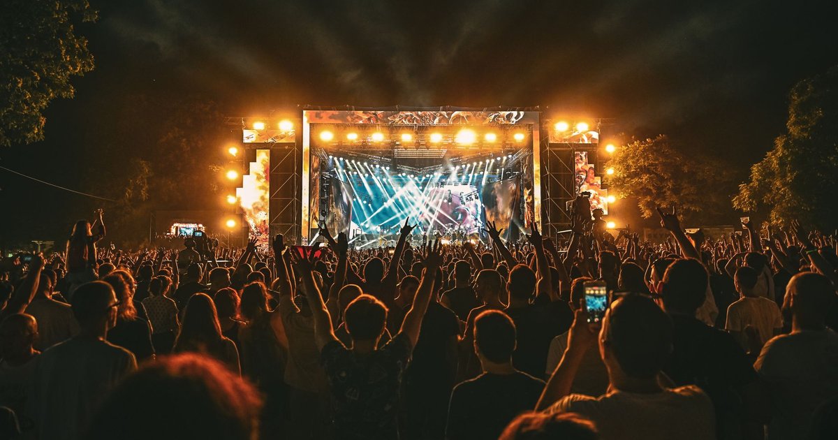 Foule en plein concert d'été, mains levées sous les lumières de scène