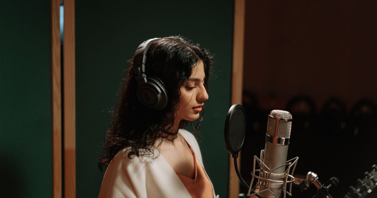 Chanteuse au casque enregistrant sa voix devant un micro dans un studio, éclairage tamisé