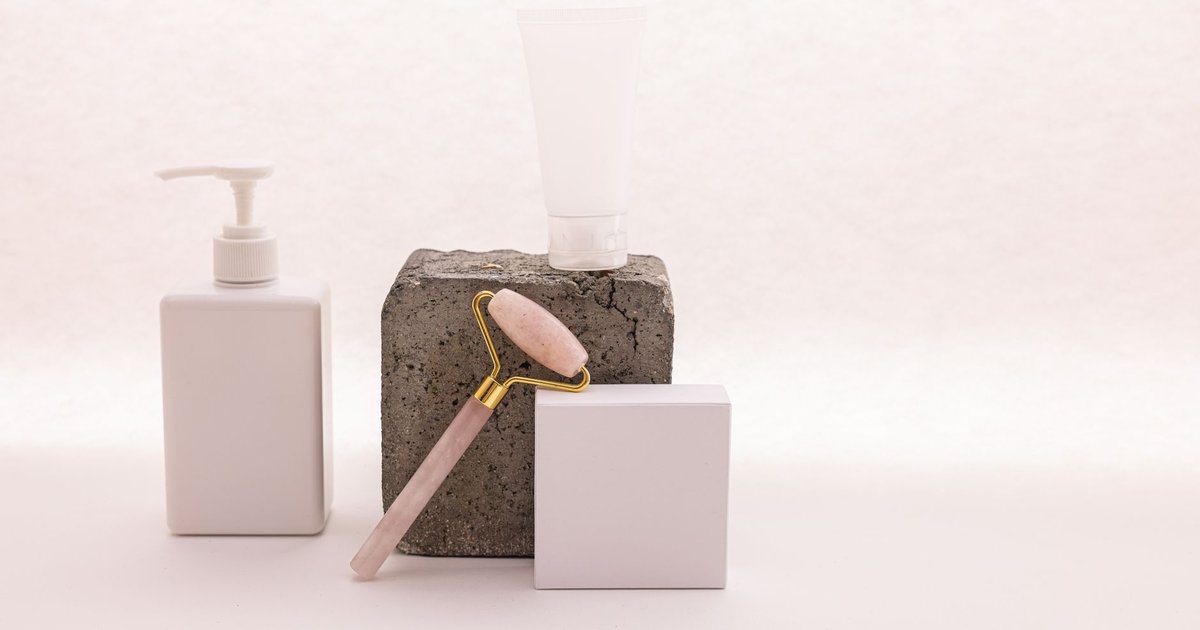 Flacon pompe, tube de soin et rouleau de massage posés sur un bloc de béton, décor beauté minimaliste