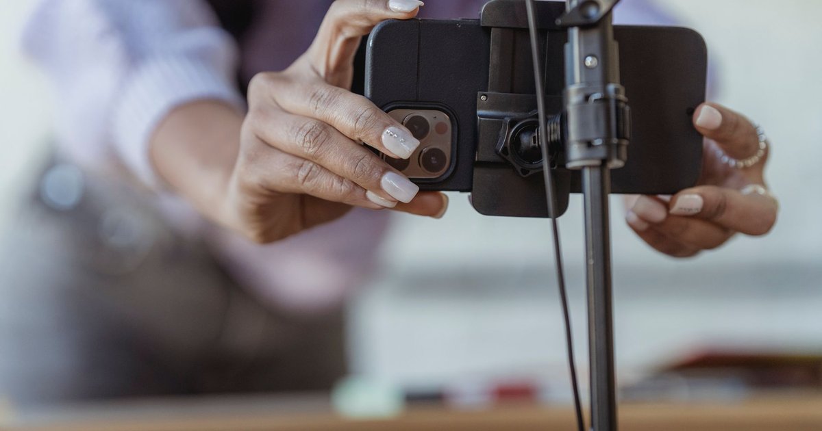 Mains d’une créatrice installant un smartphone sur un trépied pour filmer une vidéo verticale