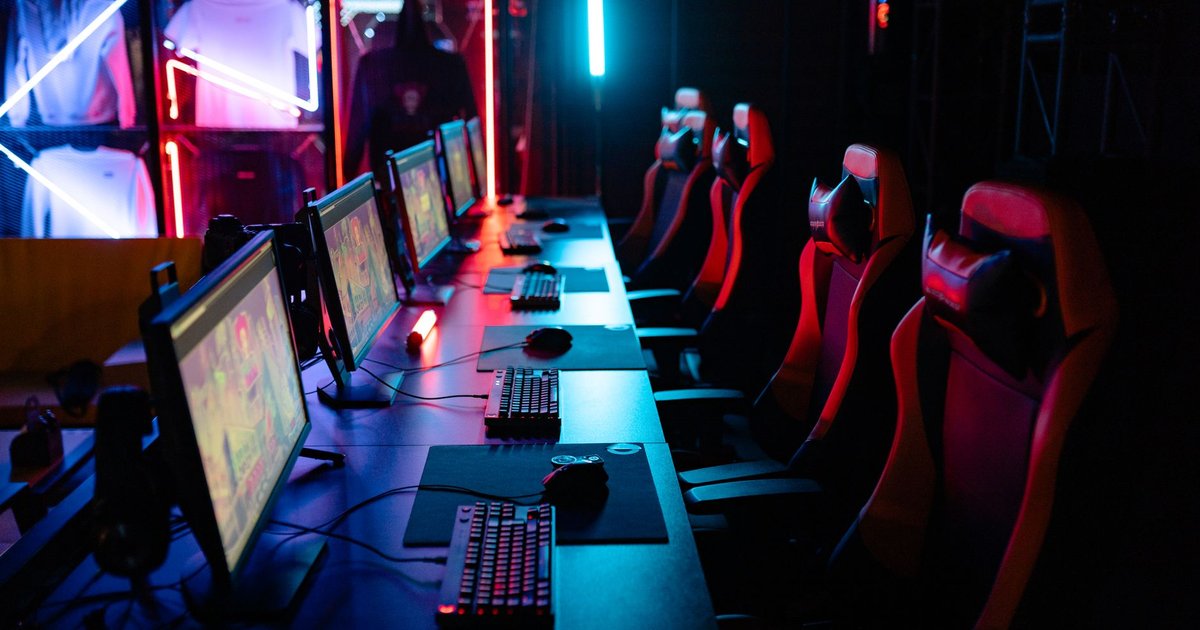 Salle d'esport éclairée aux néons rouges et bleus, avec une rangée d'écrans de jeu et de sièges gamer
