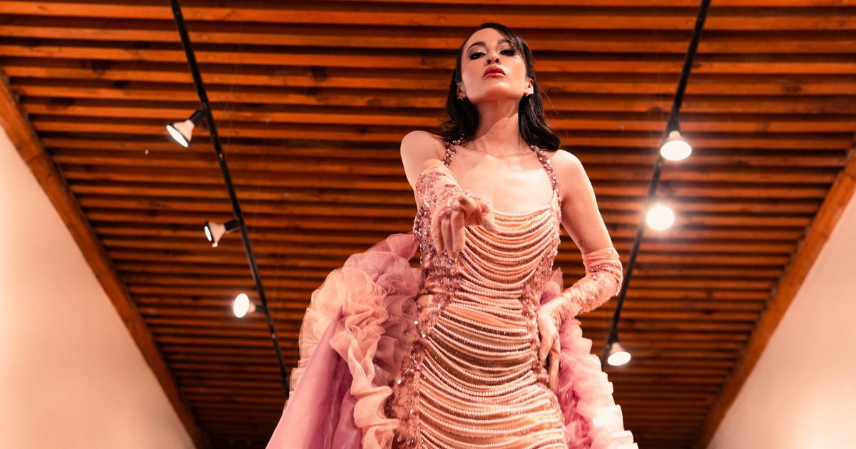 Mannequin en robe rose pâle drapée défilant sous les projecteurs lors d'un défilé de mode luxe.