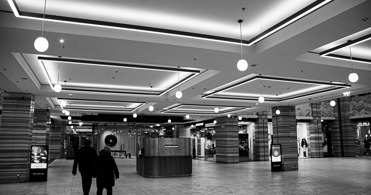 Intérieur d'un centre commercial moderne en noir et blanc, avec des totems d'affichage numérique et deux passants