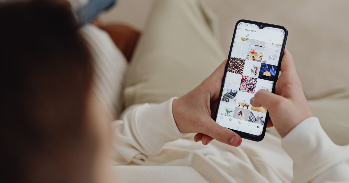 Personne qui fait défiler une grille de photos sur un réseau social depuis son smartphone, assise dans un canapé