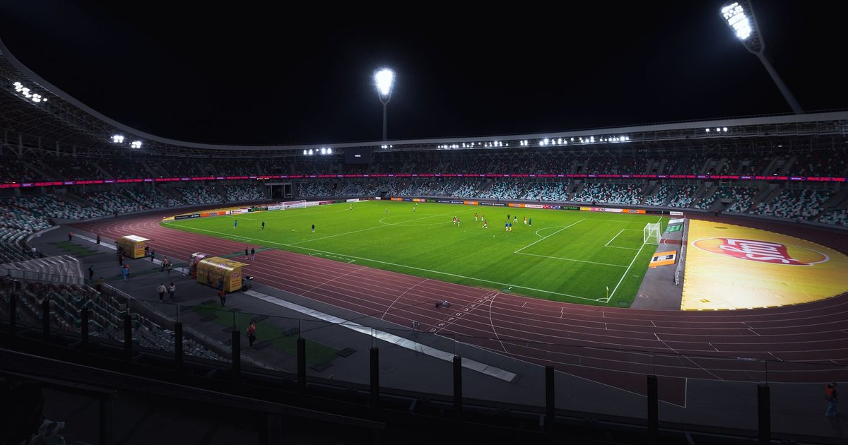 Stade de football illuminé la nuit par ses projecteurs, tribunes clairsemées autour de la pelouse